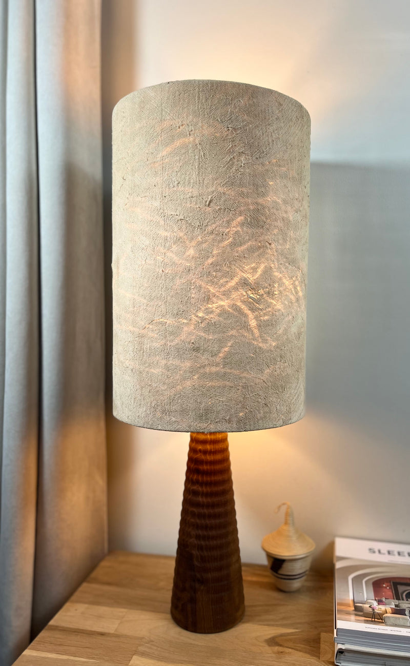Lampe illuminée en tissu d'écorce d'arbre avec pied en bois tourné, posée sur une table de chevet avec des magazines